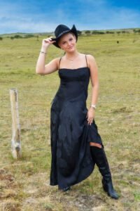 Meisje in natuurachtergrond draagt Midnight Rose Satin Dress en zwarte cowboyhoed