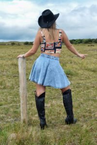 Model met rug naar camera, natuurachtergrond met dieren in de verte, draagt Wanted & Wild Top, Rodeo Drive Denim Skirt en Midnight Western Boots, zwarte cowboyhoed