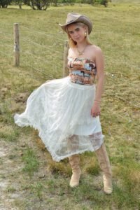 Model in natuurachtergrond, draagt Wild Horse Spirit Top, Wildflower Lace Skirt, Southern Trail Boots en beige cowboyhoed